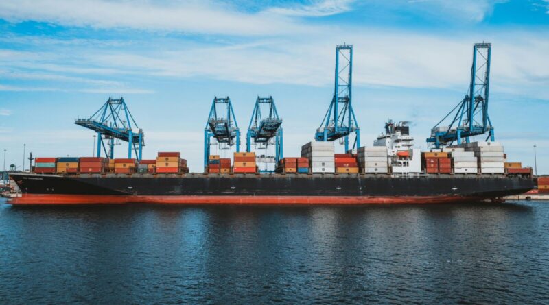 Large cargo ship with colorful metal containers floating on rippling water of ocean under cloudy blue sky in daylight