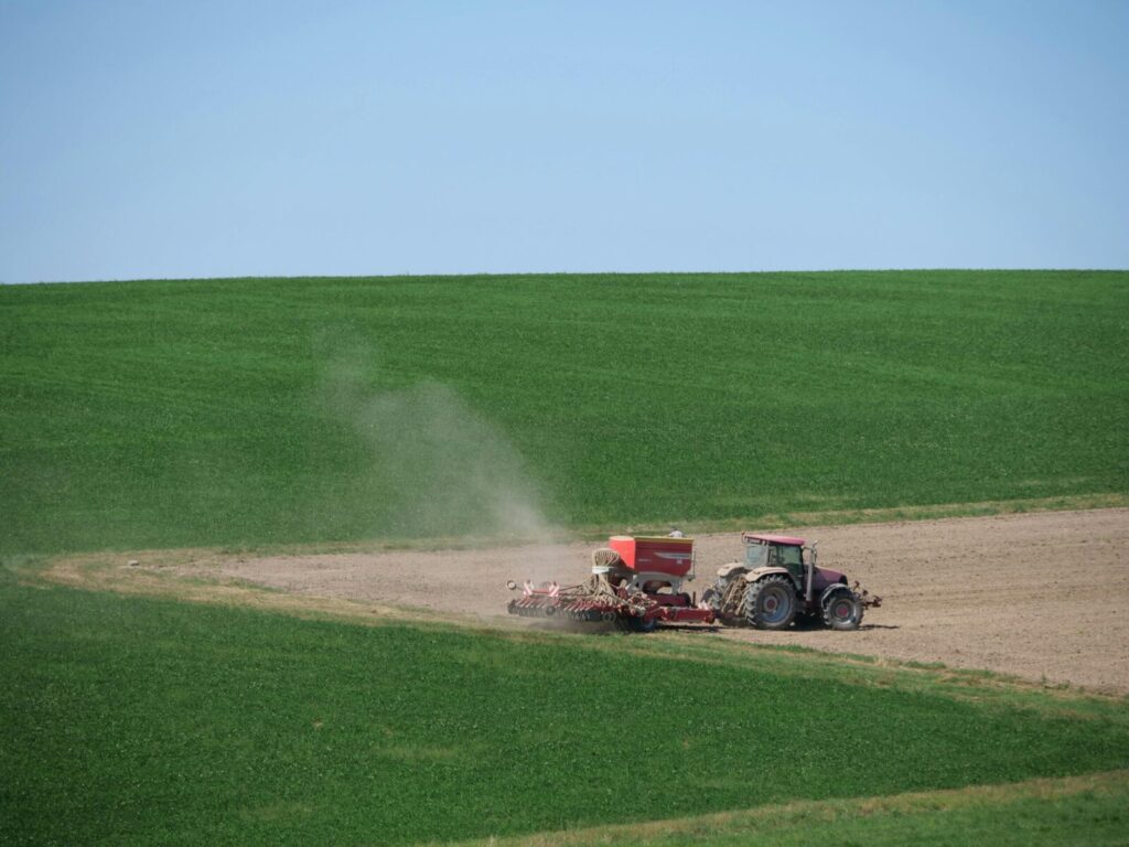Tractor plowing a vast green field under blue sky, showcasing modern farming techniques.