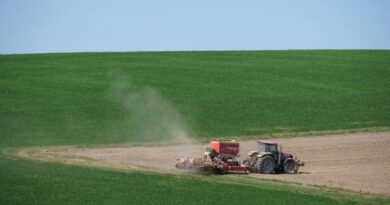Tractor plowing a vast green field under blue sky, showcasing modern farming techniques.