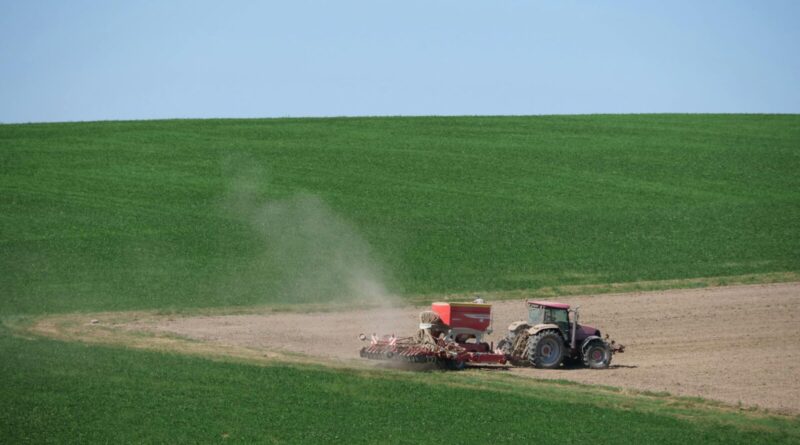 Tractor plowing a vast green field under blue sky, showcasing modern farming techniques.