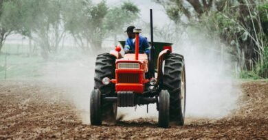 A man rides a red tractor while plowing a dusty field, showcasing agriculture and farming equipment.