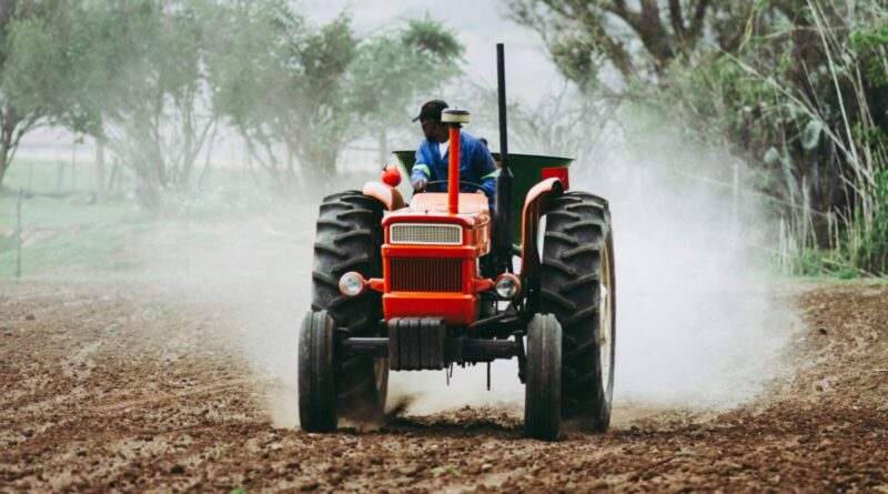 A man rides a red tractor while plowing a dusty field, showcasing agriculture and farming equipment.